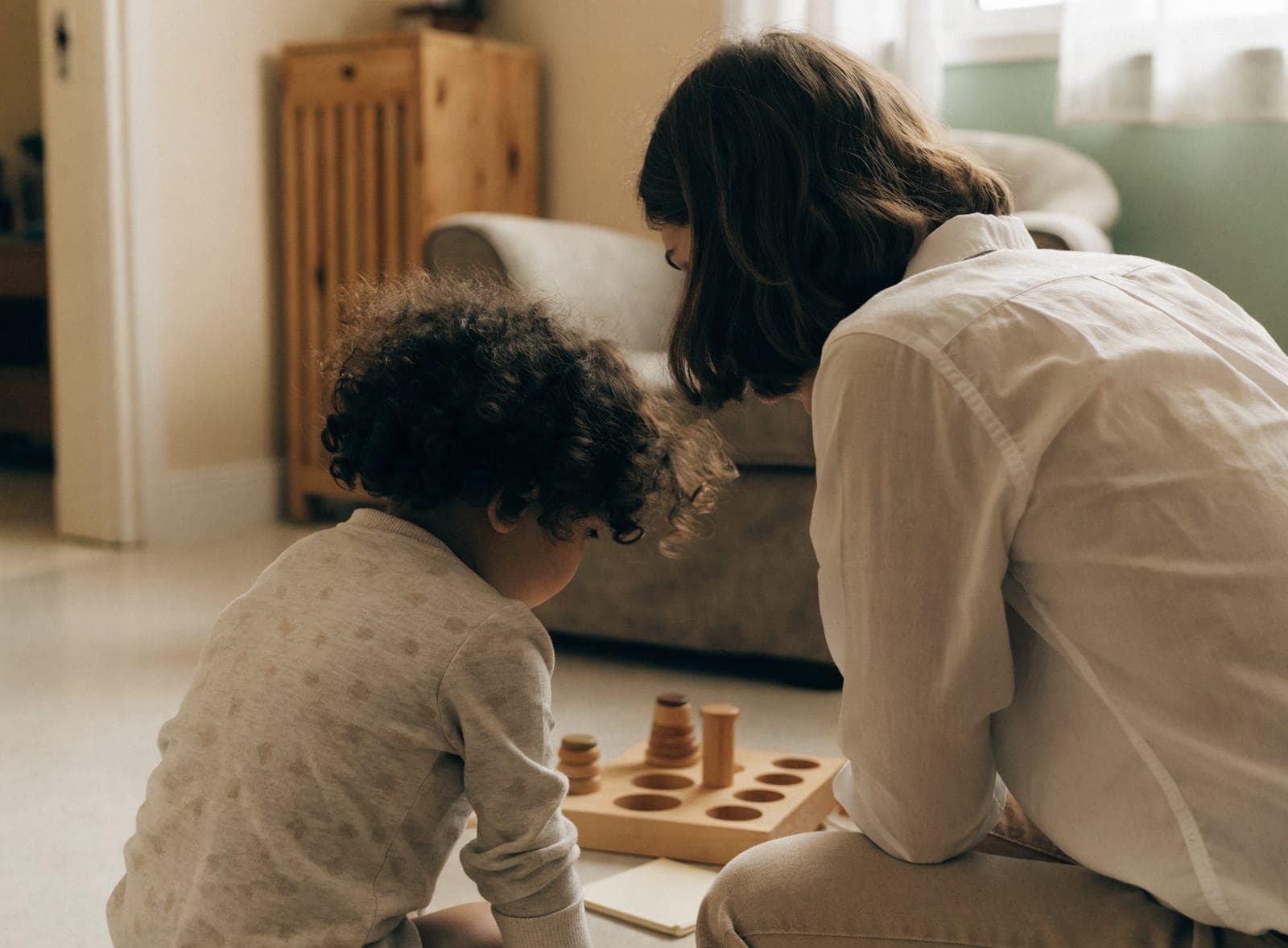 A behavior specialist guiding a child through an activity with a wooden learning toy at home.