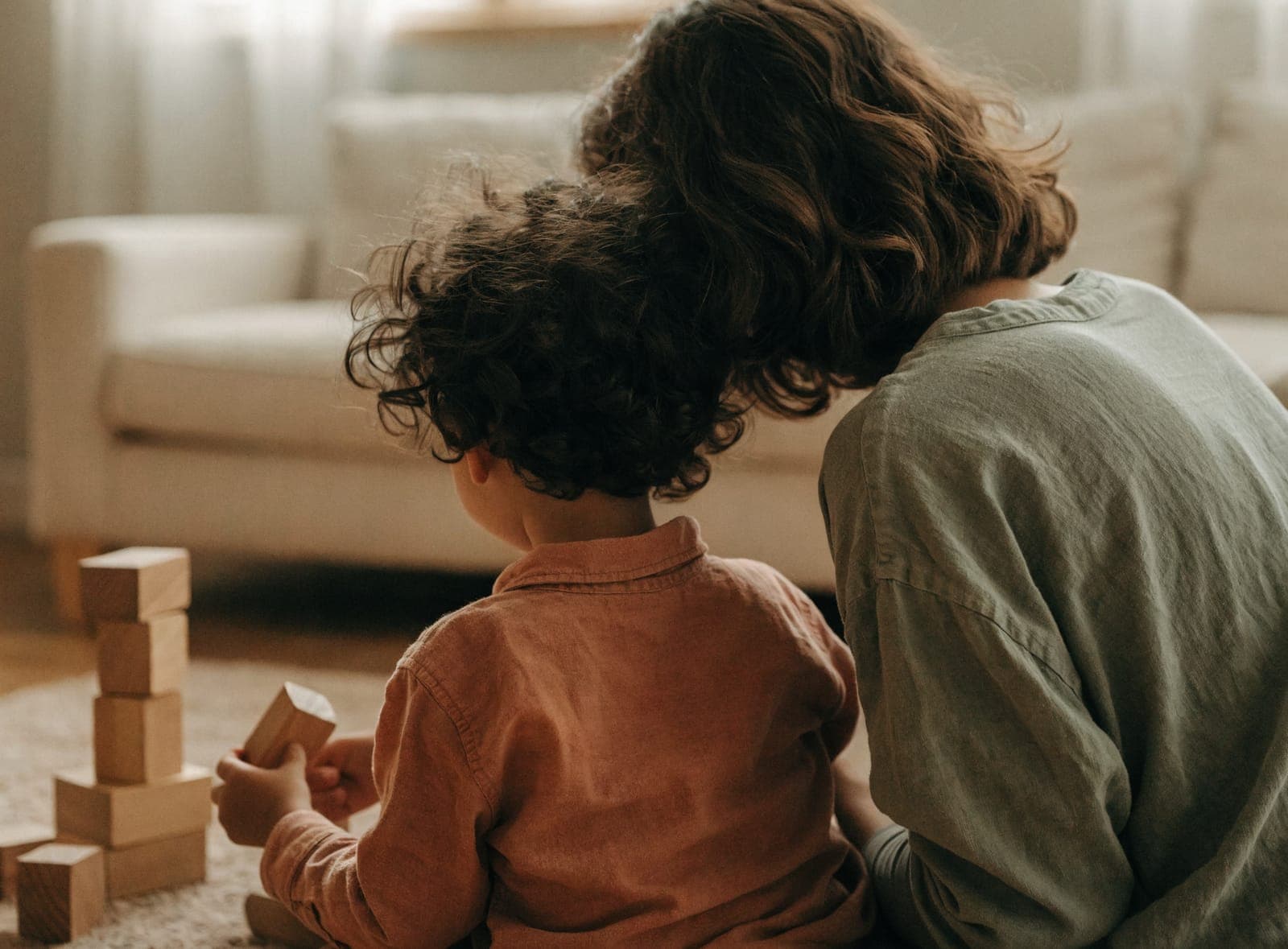 A parent and child playing with wooden blocks on a rug at home.